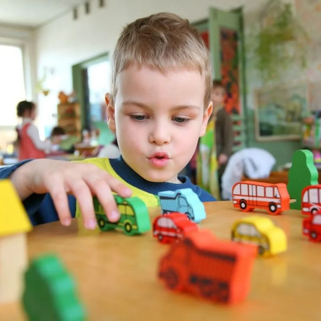 Stock photo of young boy playing with colorful wooden toy vehicles on a classroom table